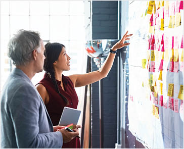 Man and woman looking at colorful adhensive notes on whiteboard in creative studio